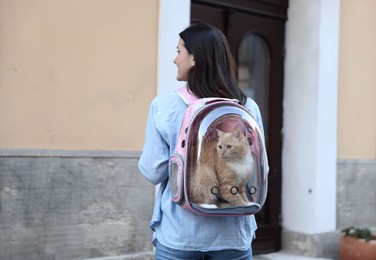 Photo of Woman with her cute cat in backpack carrier on city street, back view