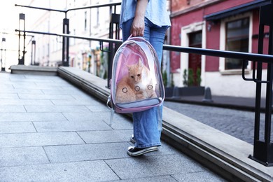 Photo of Woman with her cute cat in backpack carrier on city street, closeup
