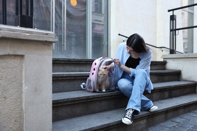 Photo of Woman with her cute cat in backpack carrier on stairs outdoors