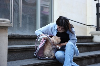 Photo of Woman with her cute cat in backpack carrier on stairs outdoors
