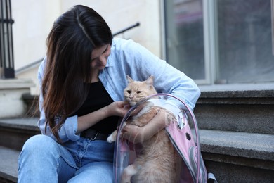 Photo of Woman with her cute cat in backpack carrier on stairs outdoors