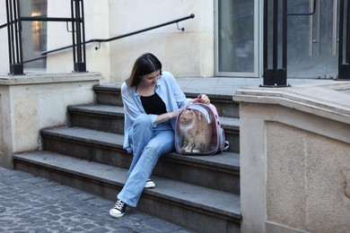Photo of Woman with her cute cat in backpack carrier on stairs outdoors