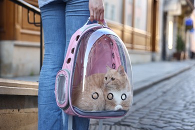 Photo of Woman with her cute cat in backpack carrier on city street, closeup