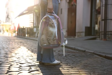 Photo of Woman with her cute cat in backpack carrier on city street, closeup