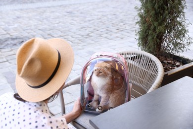 Photo of Woman with her cute cat in backpack carrier at cafe outdoors