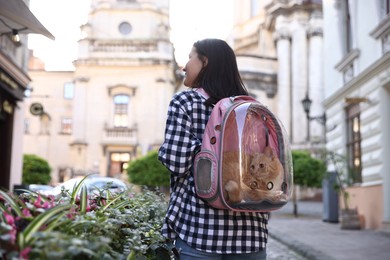 Photo of Woman with her cute cat in backpack carrier on city street, back view