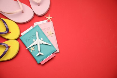 Photo of Airplane model, passports, flight tickets, flip flops and starfishes on red background, flat lay. Space for text