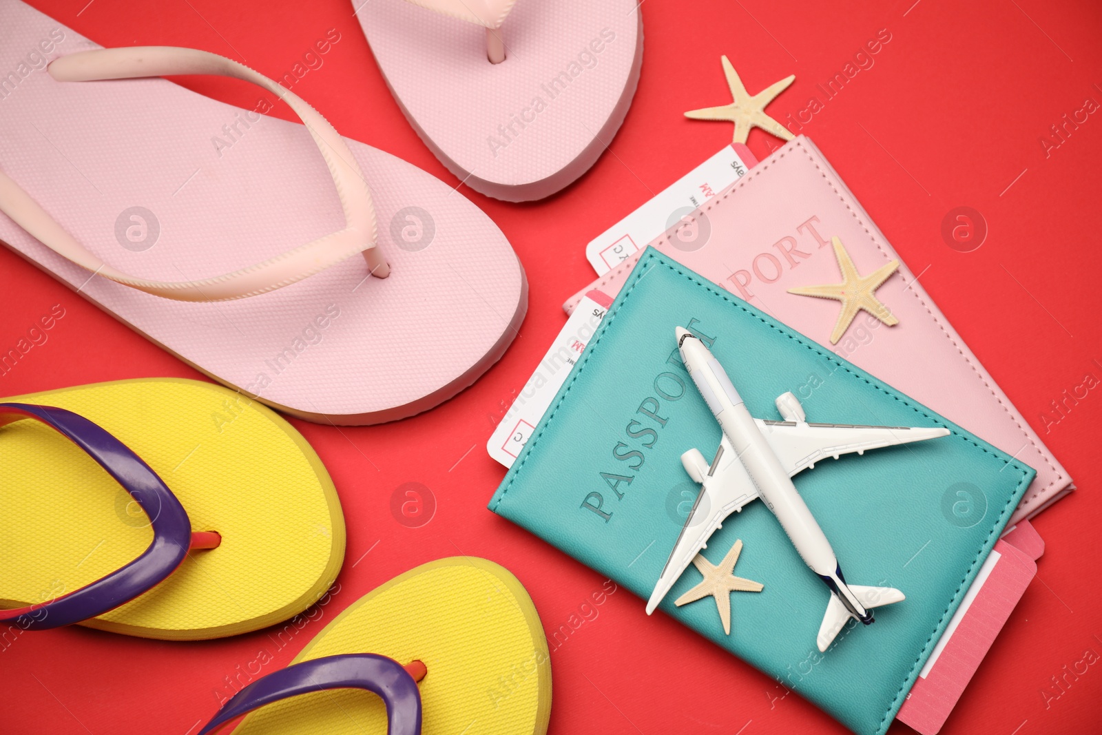Photo of Airplane model, passports, flight tickets, flip flops and starfishes on red background, flat lay
