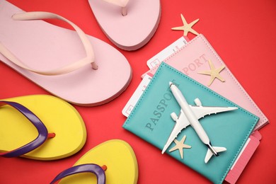 Photo of Airplane model, passports, flight tickets, flip flops and starfishes on red background, flat lay