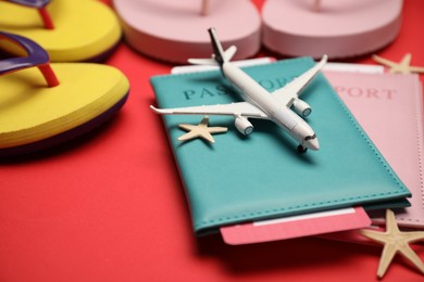 Photo of Airplane model, passports, flight tickets, flip flops and starfishes on red background, closeup