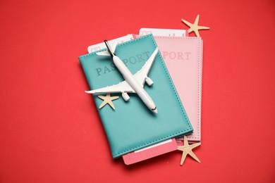 Photo of Airplane model, passports, flight tickets and starfishes on red background, above view