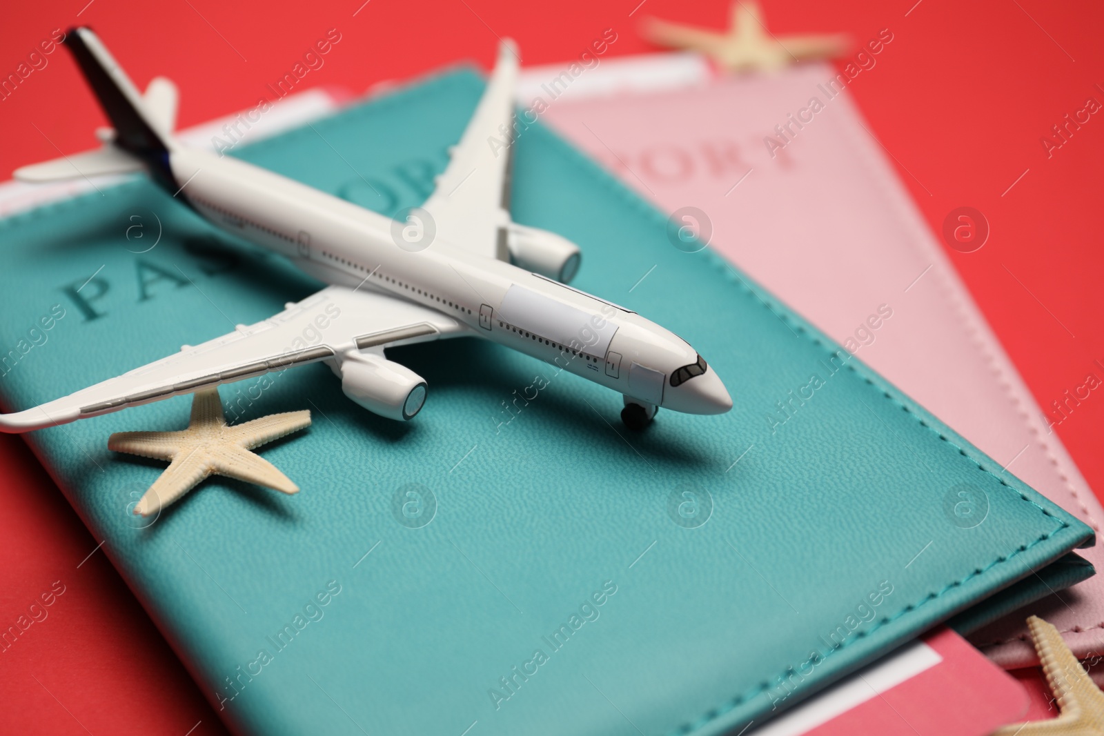 Airplane model, passports, flight tickets and starfishes on red background, closeup Photo of Airplane model, passports, flight tickets and starfishes on red background, closeup