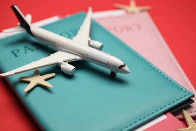Photo of Airplane model, passports, flight tickets and starfishes on red background, closeup