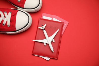 Photo of Airplane model, passport, flight tickets and sneakers on red background, flat lay