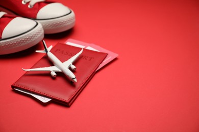 Photo of Airplane model, passport, flight tickets and sneakers on red background, closeup. Space for text
