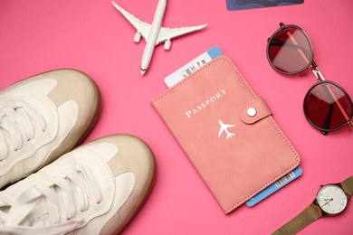 Photo of Airplane model, passport, flight ticket and accessories on pink background, flat lay