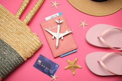 Photo of Airplane model, passport, flight ticket, credit card, and beach accessories on pink background, flat lay