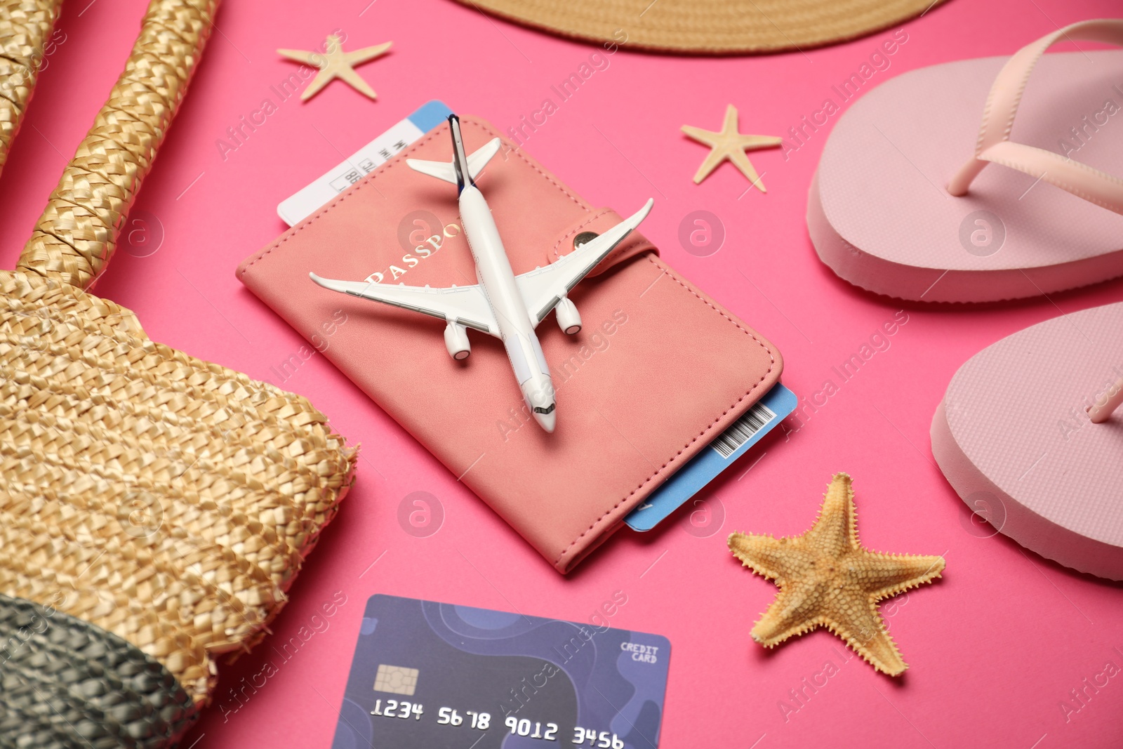 Photo of Airplane model, passport, flight ticket, credit card, and beach accessories on pink background, above view