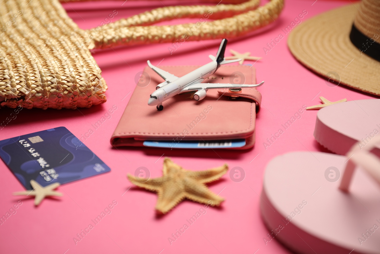 Photo of Airplane model, passport, flight ticket, credit card, and beach accessories on pink background, closeup