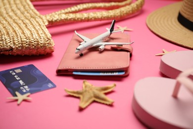 Photo of Airplane model, passport, flight ticket, credit card, and beach accessories on pink background, closeup