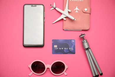Photo of Airplane model, passport, credit card, smartphone, tripod and sunglasses on pink background, flat lay