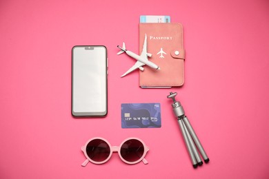 Photo of Airplane model, passport, flight ticket, credit card, smartphone, tripod and sunglasses on pink background, flat lay