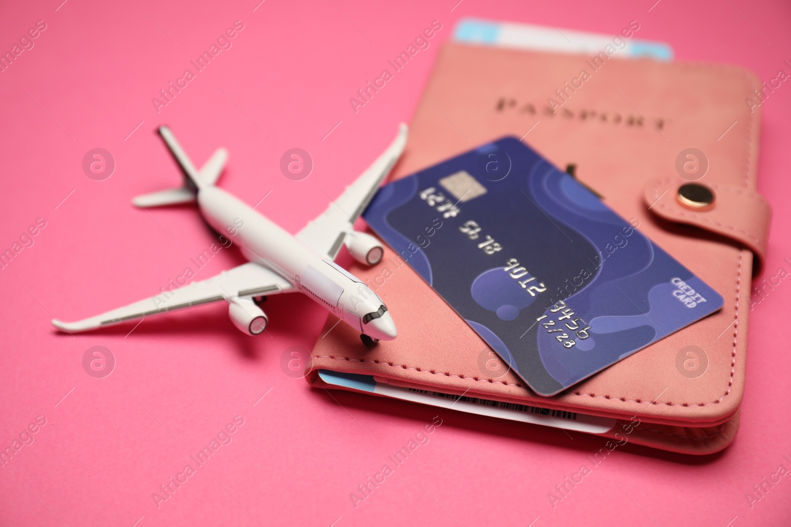 Photo of Airplane model, passport, flight ticket and credit card on pink background, closeup