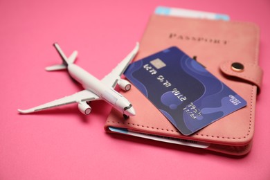 Photo of Airplane model, passport, flight ticket and credit card on pink background, closeup