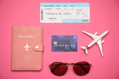 Photo of Airplane model, passport, flight ticket, credit card and sunglasses on pink background, flat lay