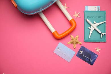 Photo of Airplane model, passport, flight ticket, credit cards, starfishes and suitcase on pink background, flat lay. Space for text