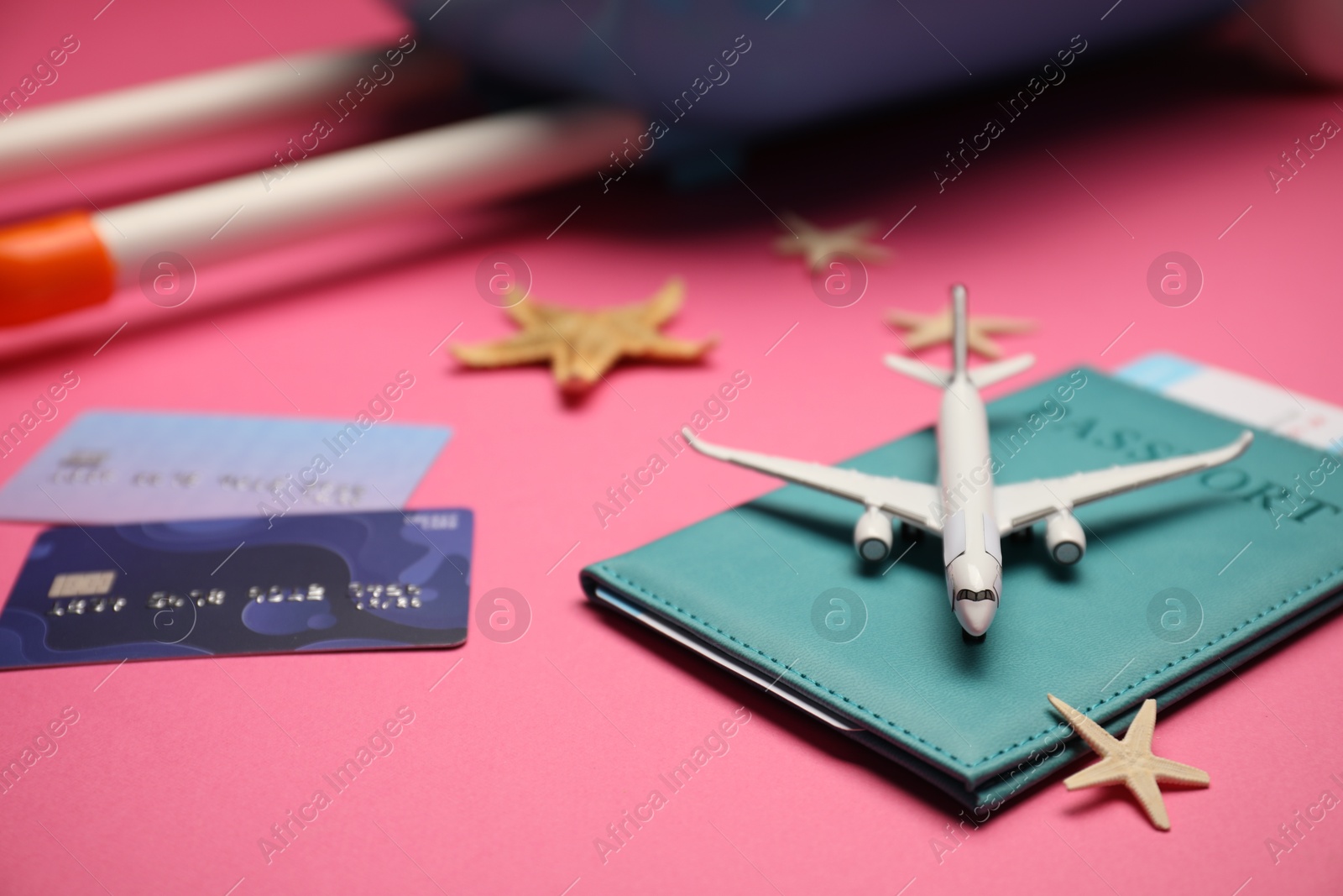 Photo of Airplane model, passport, flight ticket, credit cards, starfishes and suitcase on pink background, closeup