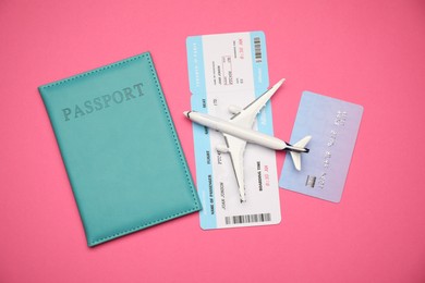Photo of Airplane model, passport, flight ticket and credit card on pink background, flat lay