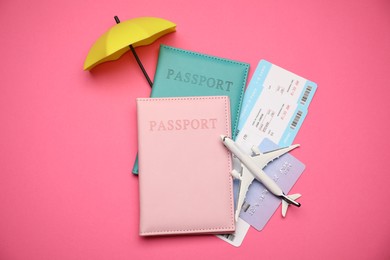 Photo of Airplane model, passports, flight tickets, credit card and small umbrella on pink background, flat lay