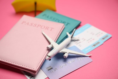 Photo of Airplane model, passports, flight tickets and credit card on pink background, closeup