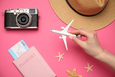 Photo of Woman with airplane model, passport, flight ticket, vintage photo camera, hat and starfishes on pink background, top view