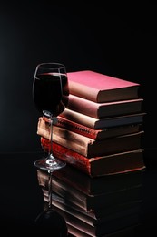 Photo of Red wine in glass and stack of books on mirror table against black background