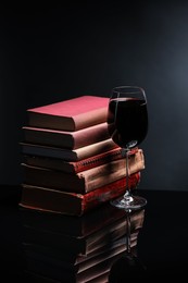 Photo of Red wine in glass and stack of books on mirror table against black background