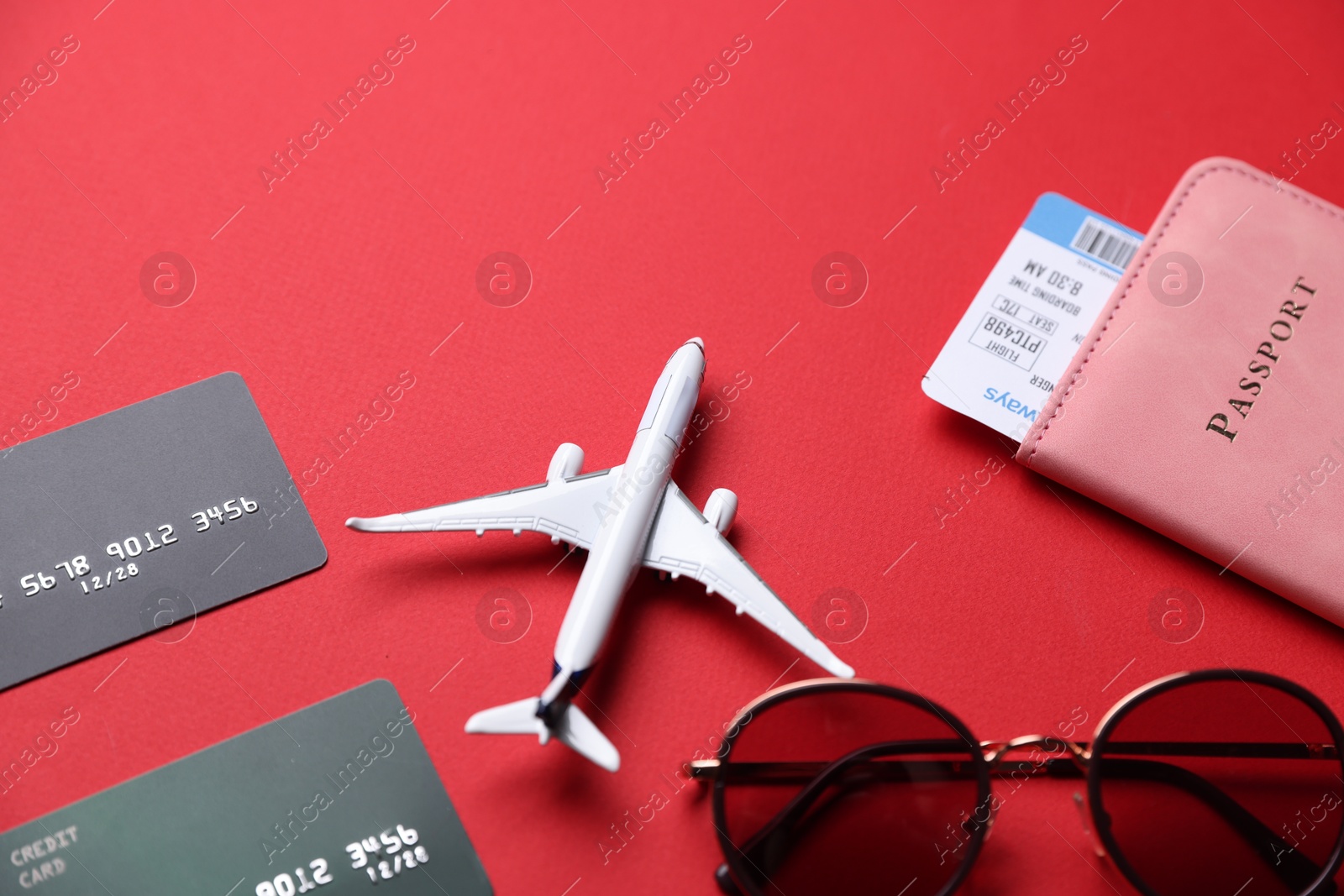 Photo of Credit cards, passport, flight ticket, airplane model and sunglasses on red background, above view