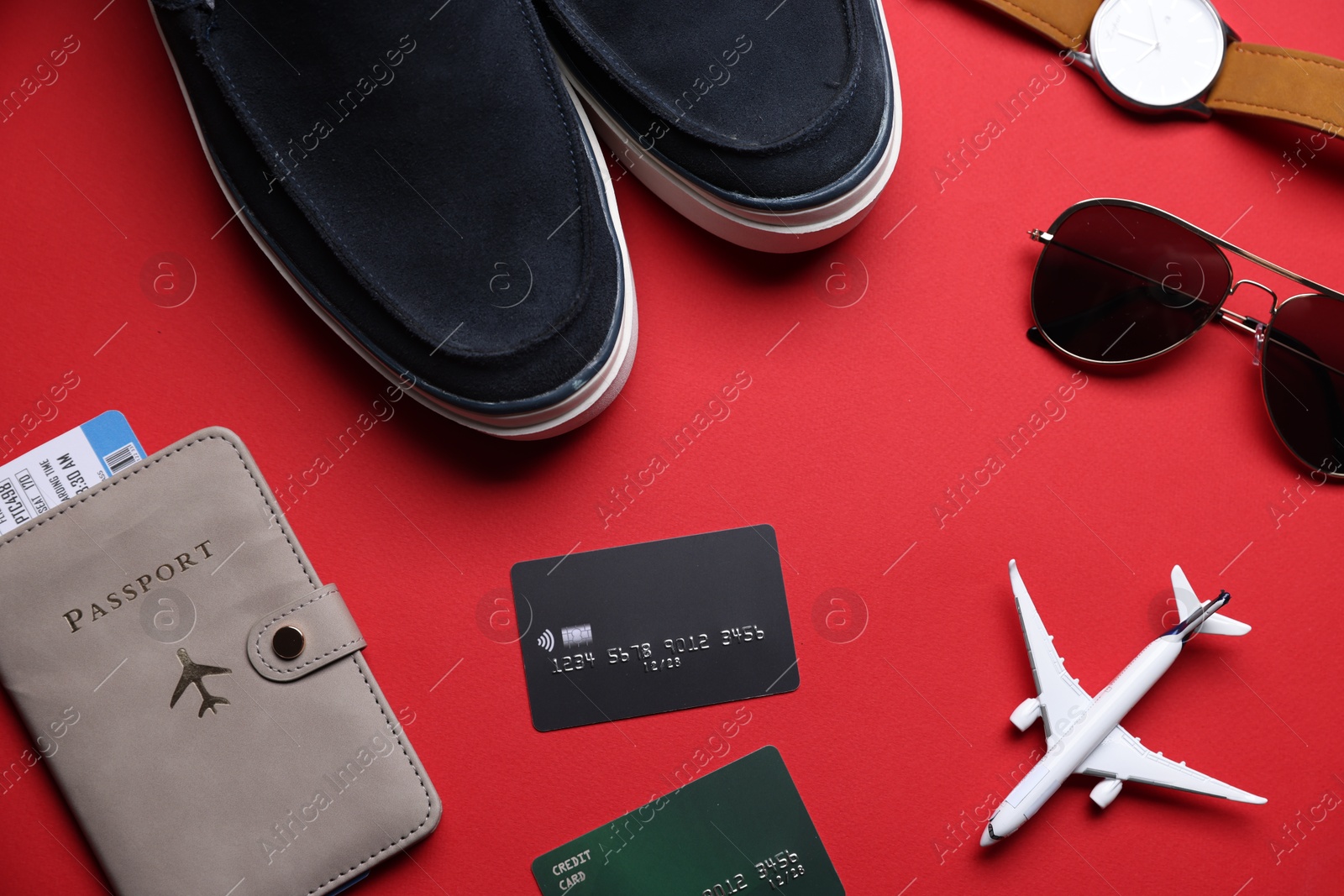 Photo of Airplane model, credit cards, passport, flight ticket, shoes and accessories on red background, flat lay