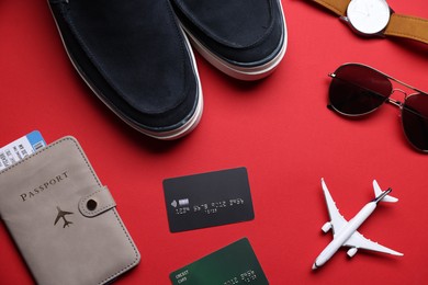 Photo of Airplane model, credit cards, passport, flight ticket, shoes and accessories on red background, flat lay