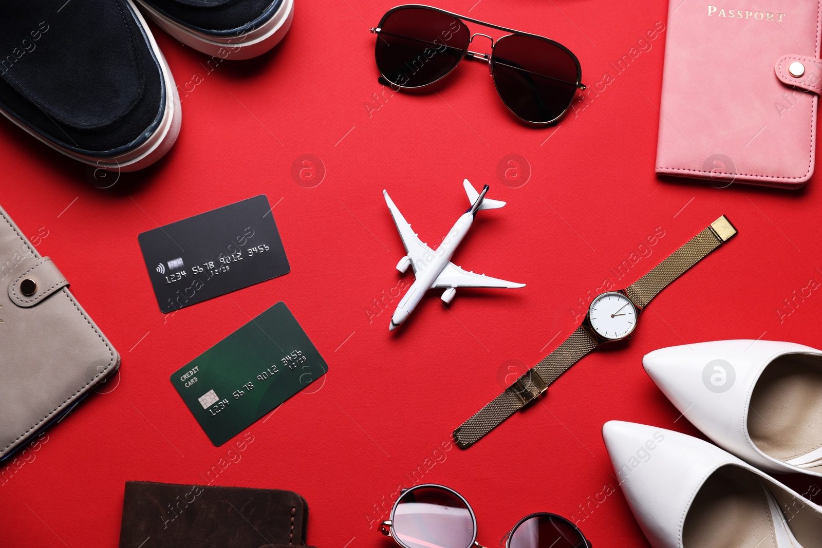 Photo of Airplane model, credit cards, passports, shoes and accessories on red background, flat lay
