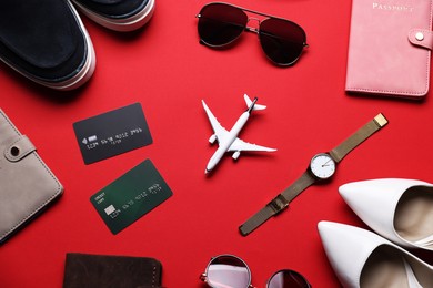 Photo of Airplane model, credit cards, passports, shoes and accessories on red background, flat lay