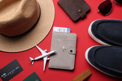 Photo of Airplane model, credit cards, passport, flight ticket, shoes and accessories on red background, flat lay