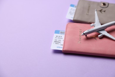 Photo of Airplane model, passports and flight tickets on violet background, closeup. Space for text