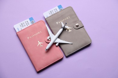Photo of Airplane model, passports and flight tickets on violet background, flat lay
