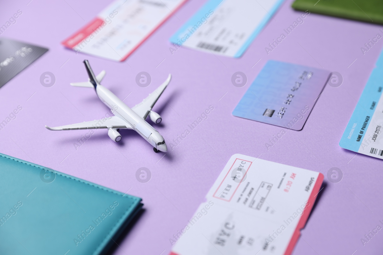 Photo of Airplane model, passport, credit card and flight tickets on violet background, closeup