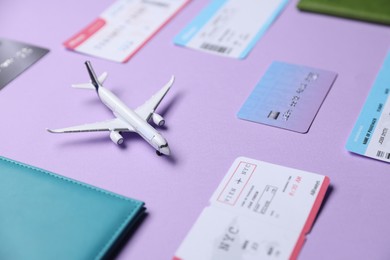 Photo of Airplane model, passport, credit card and flight tickets on violet background, closeup