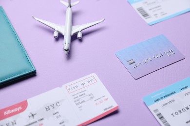 Photo of Airplane model, flight tickets, credit card and passport on violet background, above view