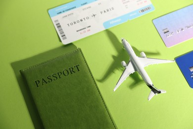 Photo of Airplane model, flight ticket, passport and credit cards on green background, flat lay