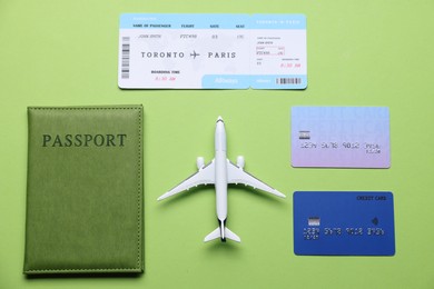 Photo of Airplane model, flight ticket, passport and credit cards on green background, flat lay